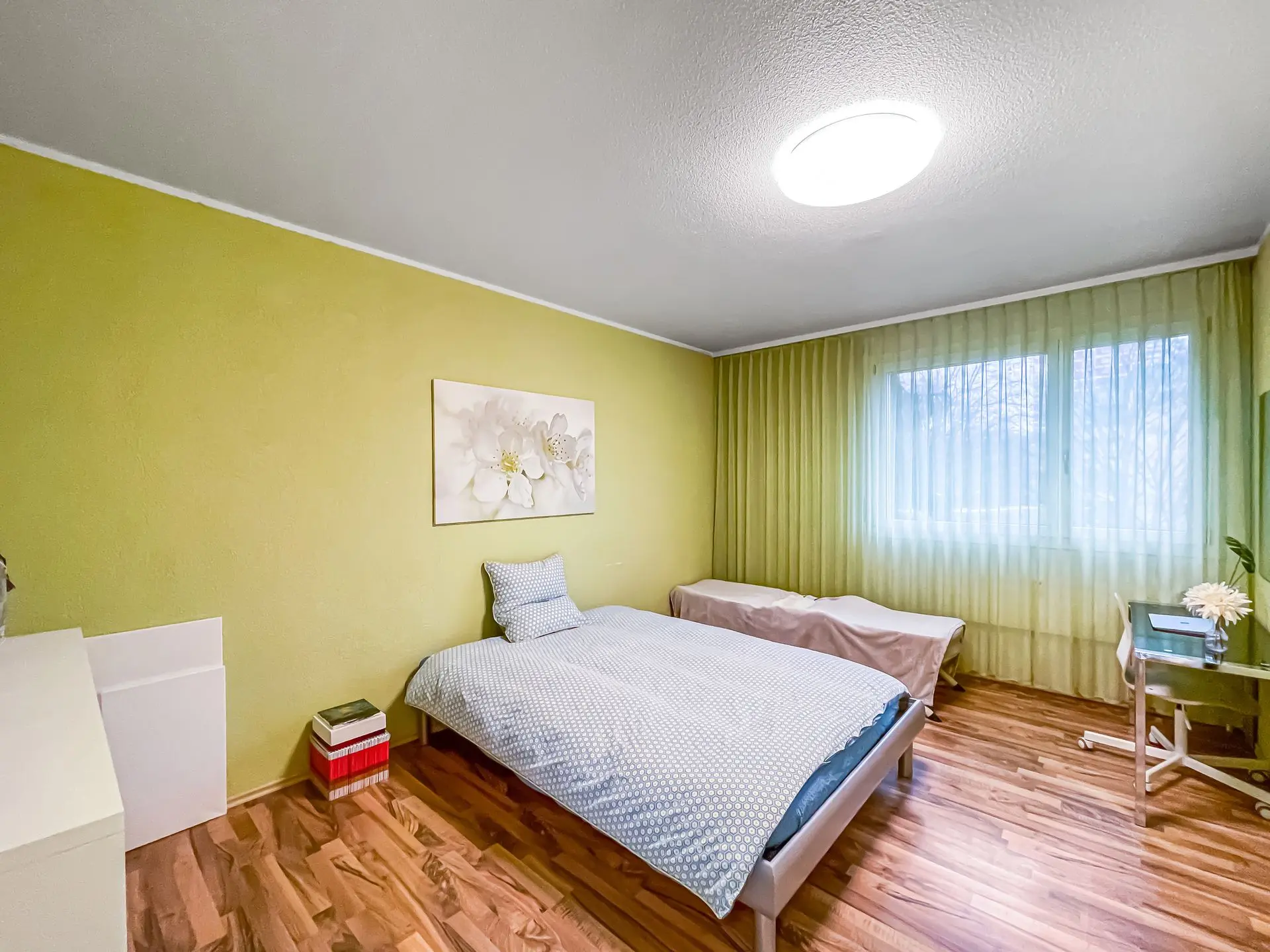 Optimierte Darstellung eines Schlafzimmers mit grün gestrichener Wand, Doppelbett und natürlichem Licht für Immobilienpräsentationen