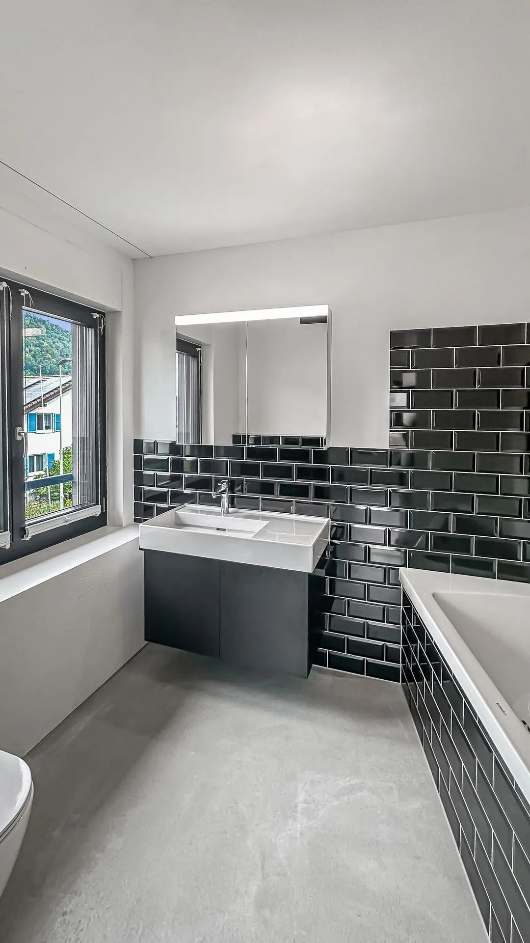 Optimiertes Foto eines Badezimmers mit schwarzer Fliesenwand, Waschbecken und Spiegel