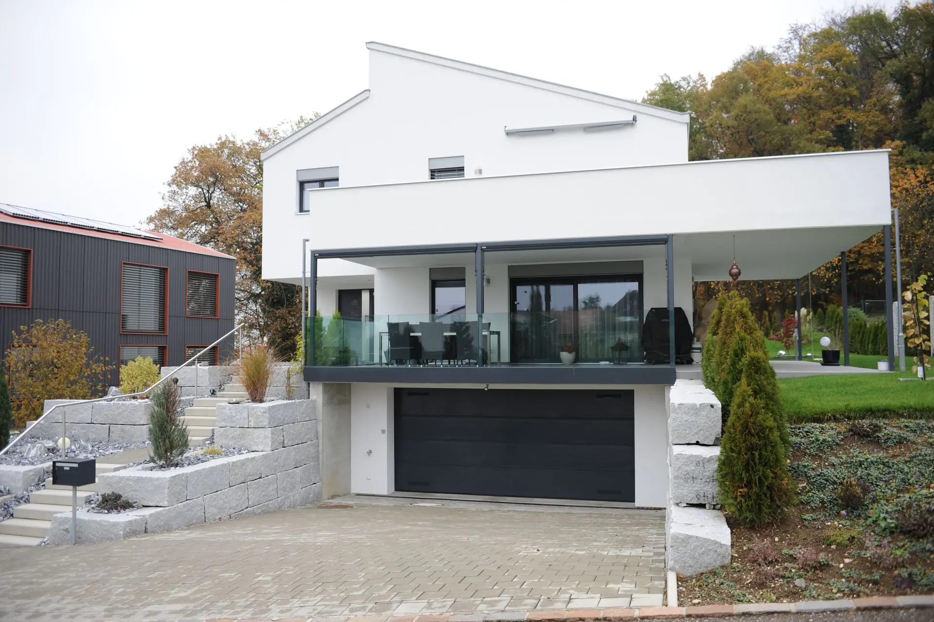 Weisses Einfamilienhaus mit Flachdach, Garage und grosszügiger Terrasse in moderner Hangbebauung