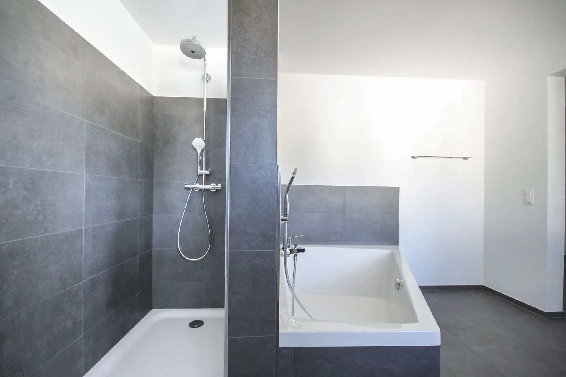 Modernes Badezimmer mit ebenerdiger Dusche und Badewanne in Grau-Weis-Optik