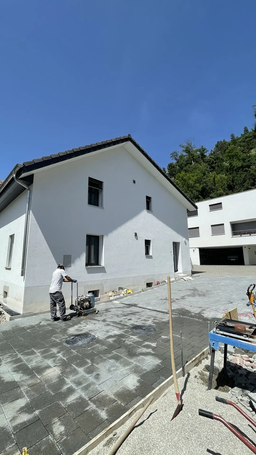 Haus mit Satteldach und frischer Fassade, Pflasterarbeiten auf der Einfahrt