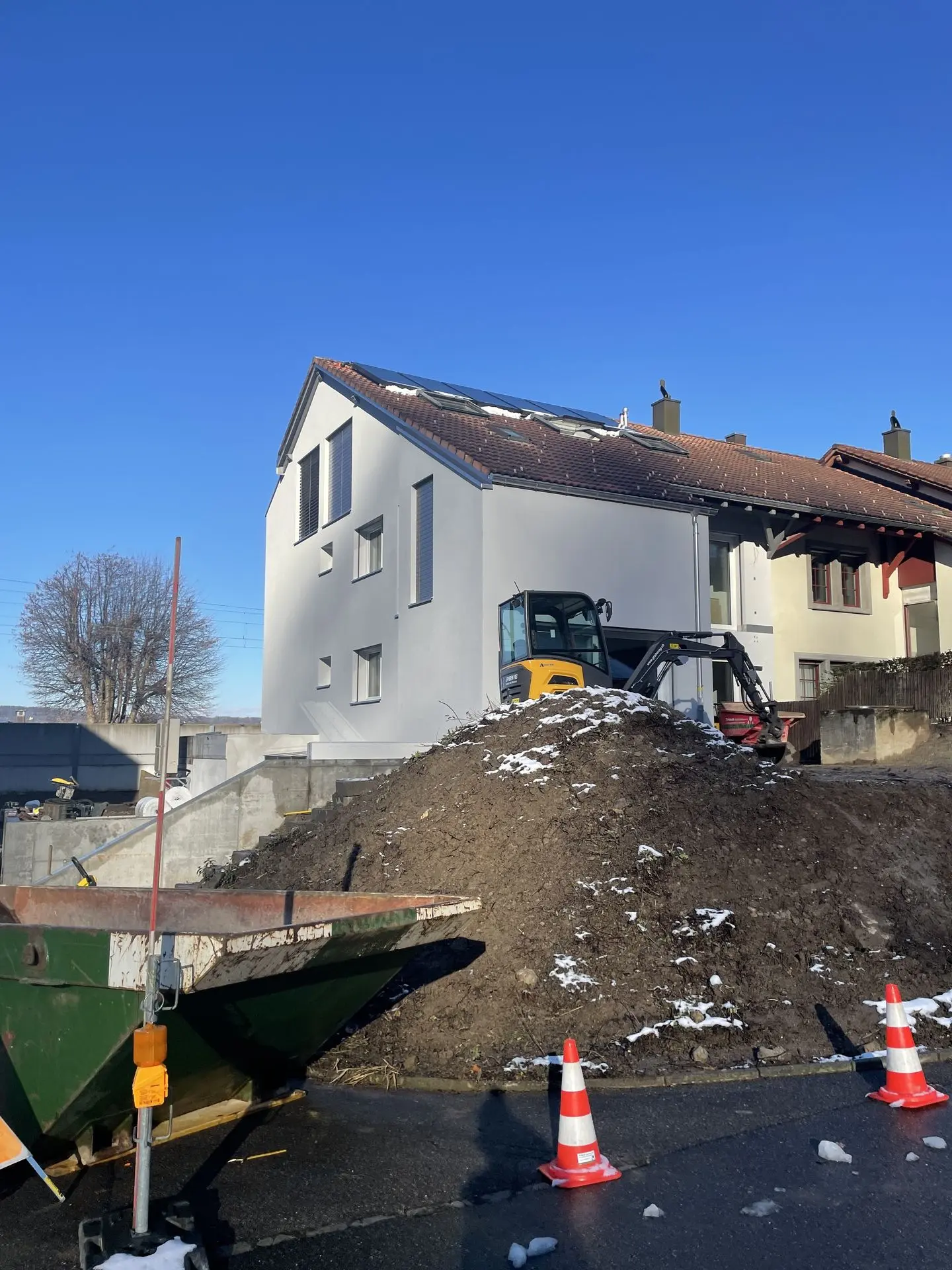 Einfamilienhaus in Bauphase mit Bagger und Erdarbeiten